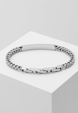 Bracelet en chaîne argentée avec des maillons épais et fins alternés, et une pièce centrale plate. Fini métallique lisse et texture polie.