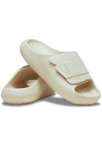 Mocassins beiges en caoutchouc, dotés d'une large sangle en tissu texturé. Design à bout ouvert et semelles à crans. Nom de la marque "crocs" visible.