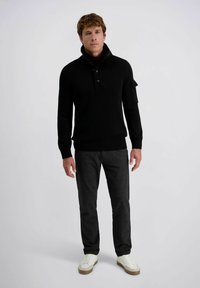 Zwarte gebreide pullover met een hoge kraag en knoopsluiting, gecombineerd met donkergrijze gebloemde broek en witte sneakers.