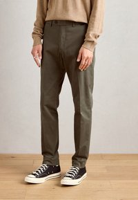 Olivgröna slim-fit chinos med framfickor och en mjuk textur, stylade med svarta sneakers och en beige tröja.