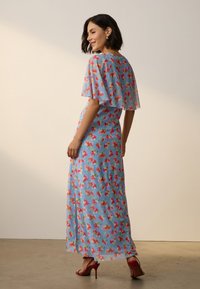 Maxikleid aus hellblauem Stoff mit einem floralen Muster in Pink und Grün. Verfügt über Flatterärmel und eine lockere Silhouette, kombiniert mit roten High Heels.