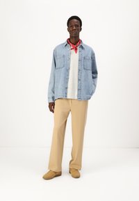 Ανοιχτό μπλε τζιν πουκάμισο με κουμπιά, το οποίο έχει επενδυθεί μ' ένα γκρι πουλόβερ, συνδυασμένο με μπεζ παντελόνι και καφέ αθλητικά παπούτσια; κόκκινο μαντήλι γύρω από τον λαιμό.