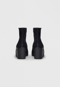 Bottines noires avec une finition en daim texturé, dotées d'un talon épais et d'une fermeture à glissière sur le côté.