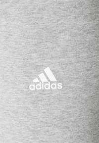 Grå bomullsblandningstyg med en jämn yta, som har en vit "adidas"-logotyp och emblem med tre ränder.