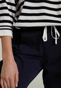 Striped sweater in white and navy, with a relaxed fit and ribbed cuffs. Paired with navy pants featuring an adjustable drawstring waist.