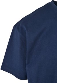 Gros plan d'un t-shirt en coton bleu marine uni à manches courtes montrant l'épaule, la manche et l'encolure.