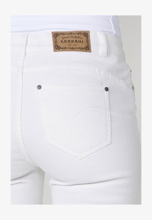 Valged denim teksad pruunist nahast sildiga, millel on kiri "KOROSHI." Omab joonistatud tagataskuid ja diskreete õmblusdetailid.