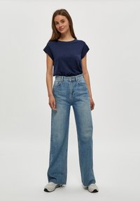 Camiseta de cuello redondo en navy con mangas enrolladas, combinada con unos pantalones vaqueros de pierna ancha de talle alto en azul claro. Zapatillas grises y blancas completan el look.