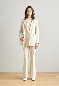 Blazer a righe e pantaloni a zampa in morbidi colori pastello. Tessuto texturizzato con un leggero lucido. Occhiali da sole oblunghi e una piccola borsa a spalla.