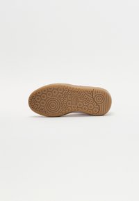 Sole tenisky z gumového materiálu s texturovaným kruhovým vzorem. Barva je světle hnědá s mírným leskem. Odolný design pro lepší trakci.