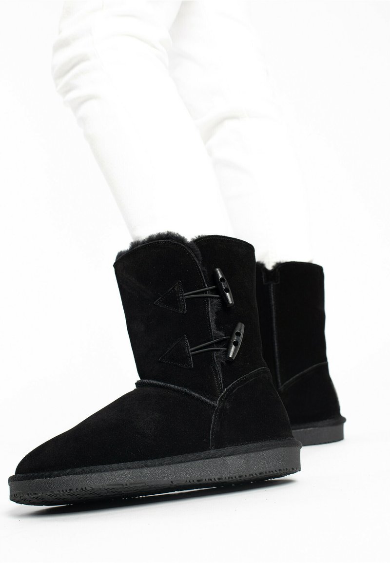 Botas de tobillo de ante negro con forro de piel de oveja, que cuentan con dos cierres de toggles negros y suela de goma texturizada negra.