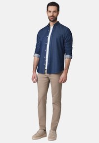 Męski strój składający się z ciemnoniebieskiej koszuli z guzikami, białego t-shirtu z okrągłym dekoltem, beżowych spodni slim-fit oraz jasnobeżowych sneakerów.