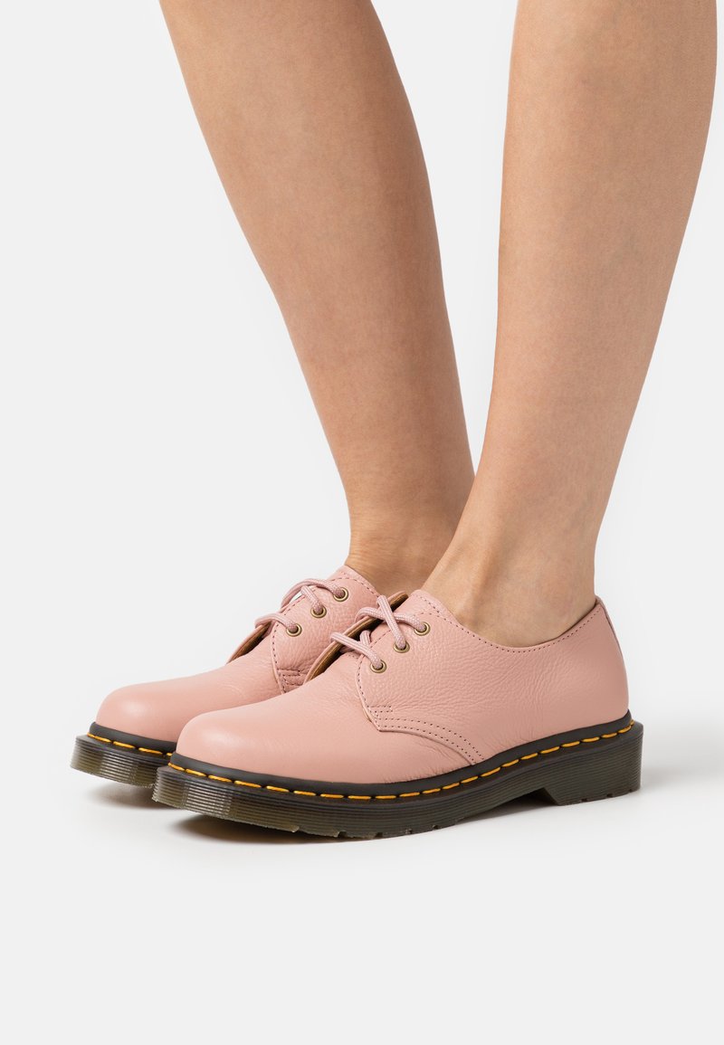 Chaussures en cuir rose à bouts ronds, avec une finition texturée, des lacets et des coutures jaunes contrastantes le long de la semelle. Design bas et robuste.