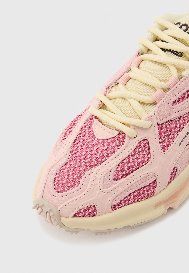 Pink and cream sneaker with textured knit fabric, cream laces, and beige sole, shown from a close-up front angle.