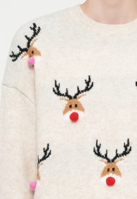 Krēmkrāsas džemperis ar atkārtotiem brūniem ziemeļbriežu sejiņām, melnām ragiem un paceltām sarkaniem vai rozā pom-pom deguniem uz pleciem un priekšpuses.