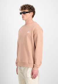 Felpa rosa chiaro con maniche lunghe e collo a giro, caratterizzata da un piccolo logo bianco sul petto e polsini a costine.