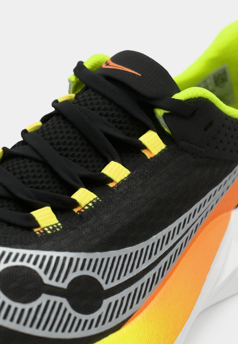 Czarny but sportowy z neonowozielonymi akcentami, posiadający siatkową cholewkę, teksturowane sznurowadła oraz wyrazistą pomarańczową podeszwę z unikalnymi wzorami.