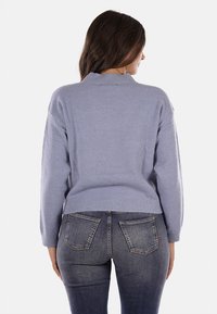 Maglione lavorato a maglia di un blu chiaro, con una vestibilità rilassata, scollo rotondo e maniche lunghe. Finitura testurizzata e orlo a coste, indossato con jeans scuri.