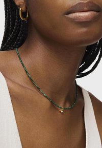 Collana di perle verdi con piccolo accento dorato e charm a forma di perla. Perle lisce in varie sfumature; attaccata a una semplice catena.