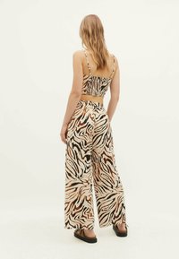 Hnědo-krémový zebra vzorovaný crop top a široké kalhoty vyrobené z lehkého materiálu, s tenkými ramínky a volným střihem.