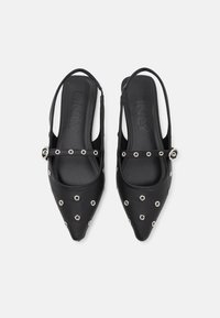 Crne slingback cipele s šiljastim prstima, s glatkom kožnom obradom i detaljima od srebrnih zakovica. Podesivi remen osigurava čvrsto prianjanje.