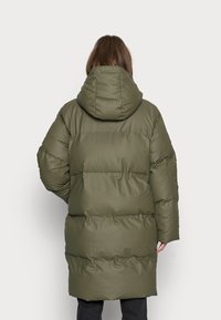 Giacca puffer verde oliva con cappuccio, caratterizzata da un design trapuntato, imbottitura spessa e una lunghezza media. Finitura liscia e opaca.