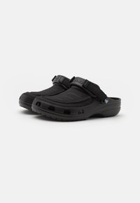 Black clogs with a textured synthetic upper, adjustable strap, and perforated sides for ventilation. Lightweight, cushioned sole enhances comfort.