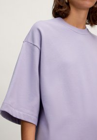 Oversized lavender T-shirt made of soft cotton blend, featuring wide sleeves and a crew neckline, with a smooth texture and minimal design.
