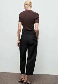 Polo shirt marrone a righe con maniche corte abbinato a pantaloni neri a vita alta, con una vestibilità rilassata e orlo alla caviglia.