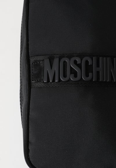 Must musta kott, millel on silmapaistev matt must "Moschino" logo. Pinna tekstuur on kareda viimistlusega ning kott on puhta, ristkülikukujulise kujuga.