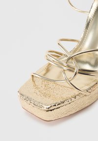 Pantof aurit cu vârf pătrat, finisaj metalic texturat, bretele decorative împletite și căptușeală interioară netedă.