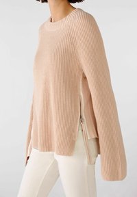 Vaaleanpunainen neulepaita, jossa on pitkät hihat, tekstuuri, sivuvetoketjut ja halkiot hemman rentoa istuvuutta varten.