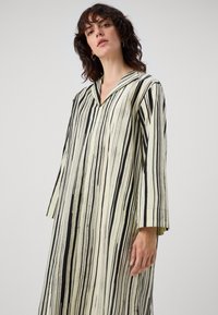 Rochie lungă, lejeră, cu dungi verticale negre și crem. Are decolteu în V și mâneci trei sferturi. Material neted, ușor.