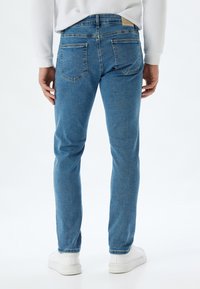 Jeans de denim azul con corte ajustado, cintura a media altura y costuras en contraste. Cuenta con dos bolsillos traseros y una etiqueta de marca en la cinturilla.