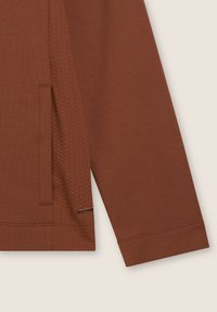 Camicia a maniche lunghe marrone con pannello laterale testurizzato e orlo cucito. Include una tasca laterale discreta e una finitura in tessuto liscia.