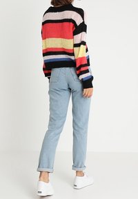 Wielokolorowy sweter w paski z czarnym tłem, z czerwonymi, żółtymi i niebieskimi paskami; zestawiony z jasnoniebieskimi dżinsami z podwiniętymi nogawkami i białymi trampkami.
