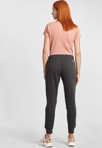 Graue Jogginghosen mit elastischen Bündchen und einem Kordelzugbund, kombiniert mit einem kurzärmligen pinken T-Shirt. Die Rückansicht zeigt eine gerade Silhouette und eine weiche Textur.