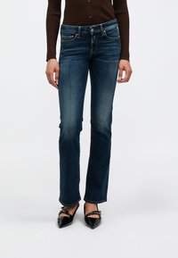 Σκούρα μπλε τζιν καμπάνα με πέντε τσέπες, ραφές και ελαφρύ ξεθώριασμα. Συνδυασμένα με μαύρα ψηλοτάκουνα παπούτσια με pointed-toe.