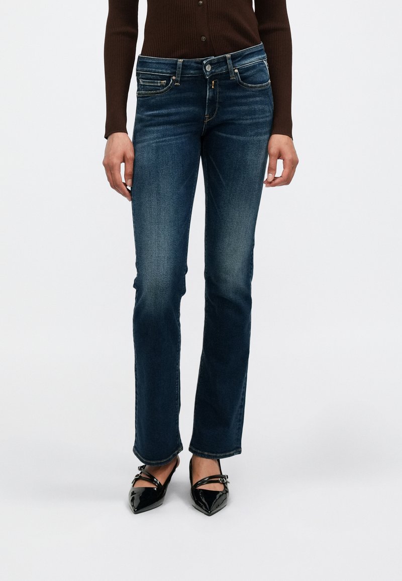 Σκούρα μπλε τζιν καμπάνα με πέντε τσέπες, ραφές και ελαφρύ ξεθώριασμα. Συνδυασμένα με μαύρα ψηλοτάκουνα παπούτσια με pointed-toe.