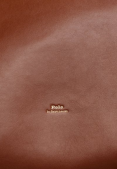 Ruskea nahkapinta, jossa on teksturoidun pinnan tuntuma. Kultaa kohotettu logo, jossa lukee "Polo by Ralph Lauren", sijaitsee alakulmassa.