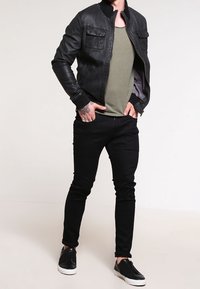 Zwarte leren bomberjack met een ritssluiting aan de voorkant, olijfgroene t-shirt en zwarte slim-fit jeans. Gecombineerd met zwarte instappers.