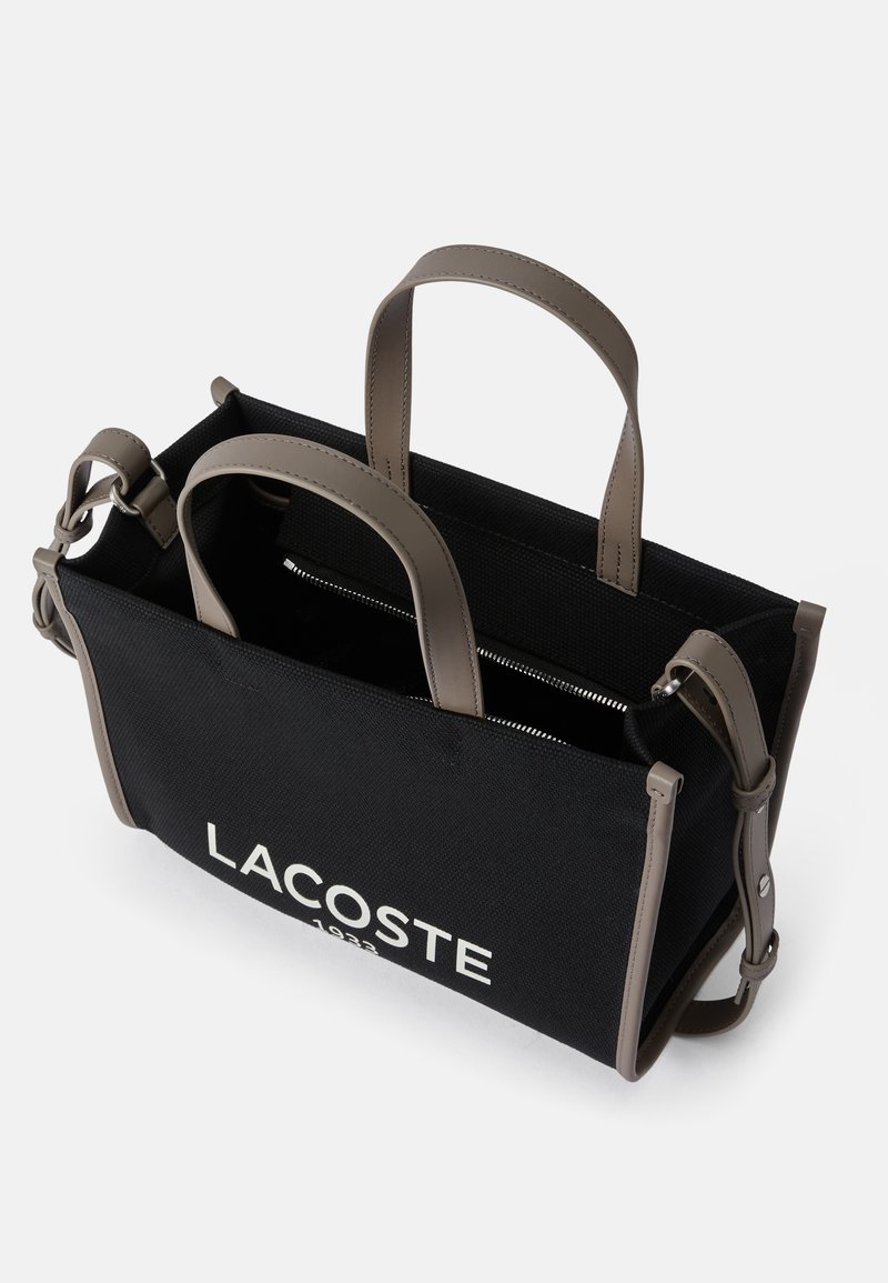 Borsa a tracolla nera in_canvas con manici in pelle grigia, caratterizzata da un logo bianco "LACOSTE" e una tasca interna con zip.