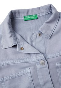 Camicia in denim azzurro chiaro con colletto a punta, chiusura a bottoni frontale e taschino sul petto, con etichetta verde "United Colors of Benetton".