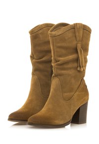 Botines de ante marrón con un diseño desgastado, punta afilada y borlas decorativas, que cuentan con un tacón apilado y cierre de cremallera.