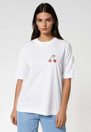 T-shirt en coton blanc à manches courtes et coupe oversize, présentant un graphique coloré de cerise sur la zone gauche de la poitrine.