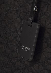 Borsa in tessuto nera con un motivo geometrico, con un'etichetta in pelle nera liscia che mostra "kate spade NEW YORK" in testo bianco.