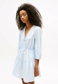 Helles blaues Kleid mit tiefem V-Ausschnitt, Dreiviertelärmel und elastischem Taillenbund. Verfügt über einen gestuften Rock und eine Kordelzugdetails.