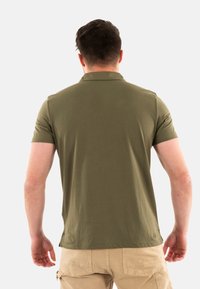 Polo shirt vert olive avec une texture unie, à manches courtes et un col classique. La chemise a une coupe droite et une couture visible en bas.