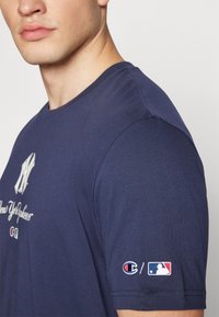 Granatowa koszulka z krótkim rękawem z białym logo Yankees na przodzie oraz haftowanymi logo Champion i MLB na rękawie.