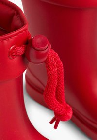 Des bottes en caoutchouc rouges avec une forme arrondie, des lacets texturés rouges et une fermeture à cordon au sommet pour un ajustement réglable.